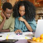 Unhappy and depressed young African-American couple calculating family budget, planning expenses, tr