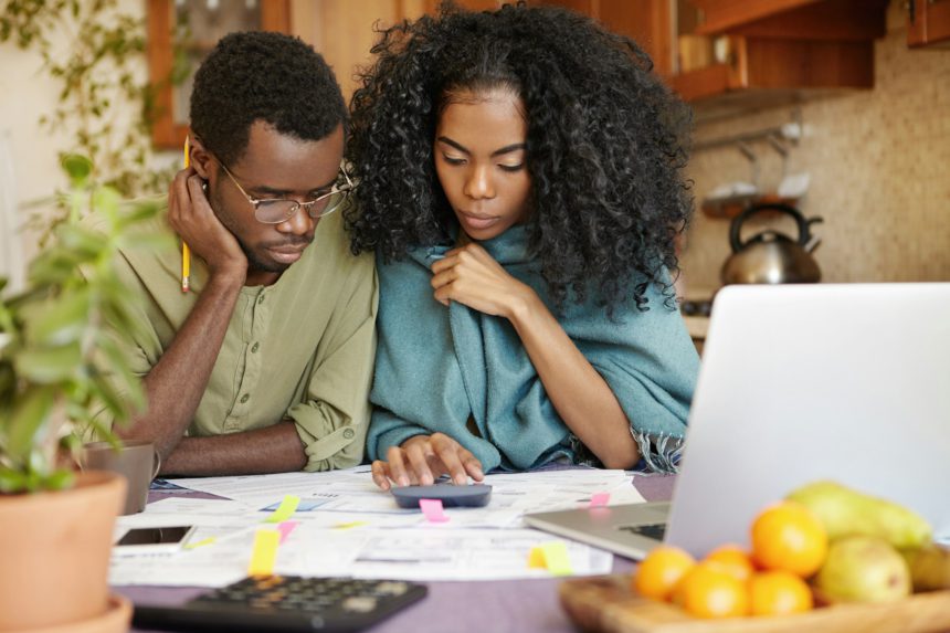 Unhappy and depressed young African-American couple calculating family budget, planning expenses, tr